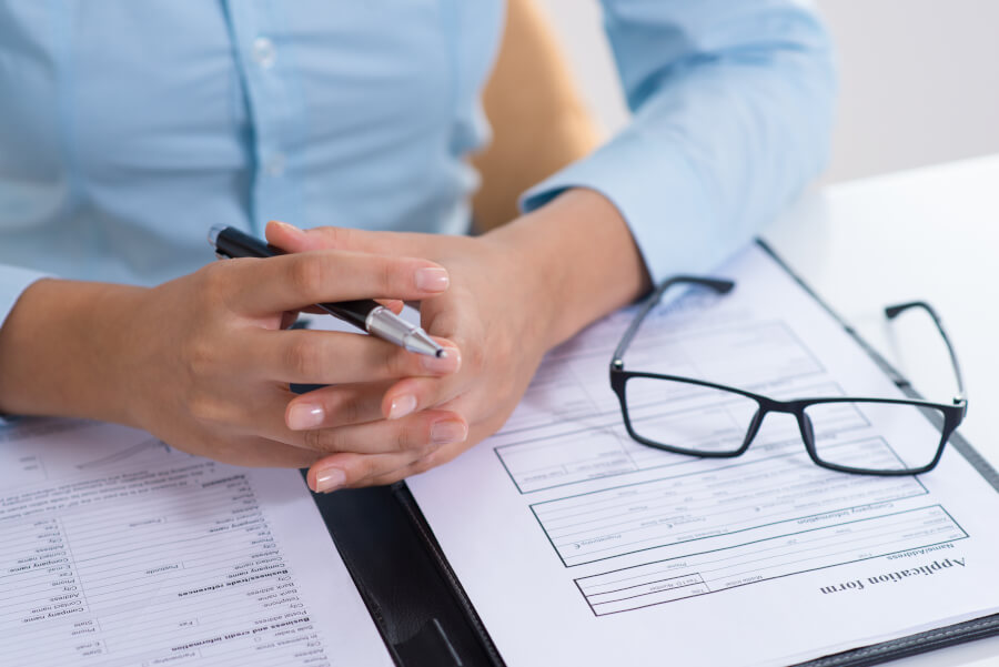 A bookkeeper at a desk in January working through a stack of vendor files beside a laptop and a calculator, checking paperwork against a list - the annual reconciliation of contractor payments against the W-9s on file before the 1099-NEC deadline