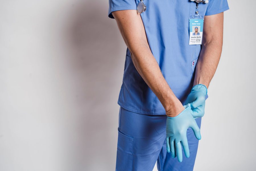 Healthcare worker in blue scrubs putting on sterile gloves in a clean clinical setting