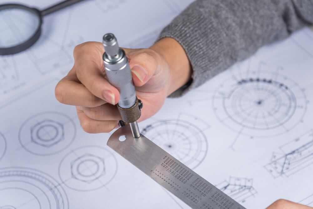 A technician checking a measuring instrument against a reference standard in a laboratory, with the calibration record open alongside