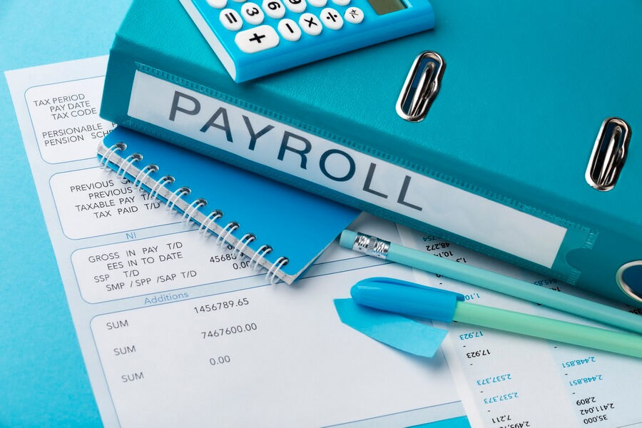 A construction payroll office reviewing the weekly certified payroll reports collected from subcontractors on a public-works project before submission