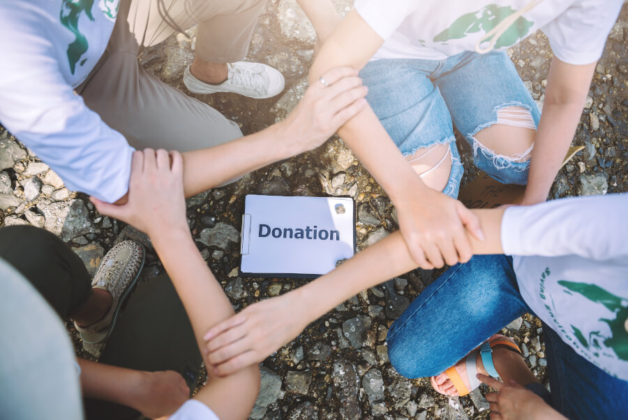 Overhead view of volunteers in matching t-shirts kneeling on gravel with their arms clasped in a circle around a clipboard reading Donation