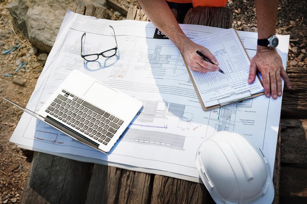 A contractor reviewing license, bond, and insurance paperwork on a job site beside a laptop tracking every renewal date