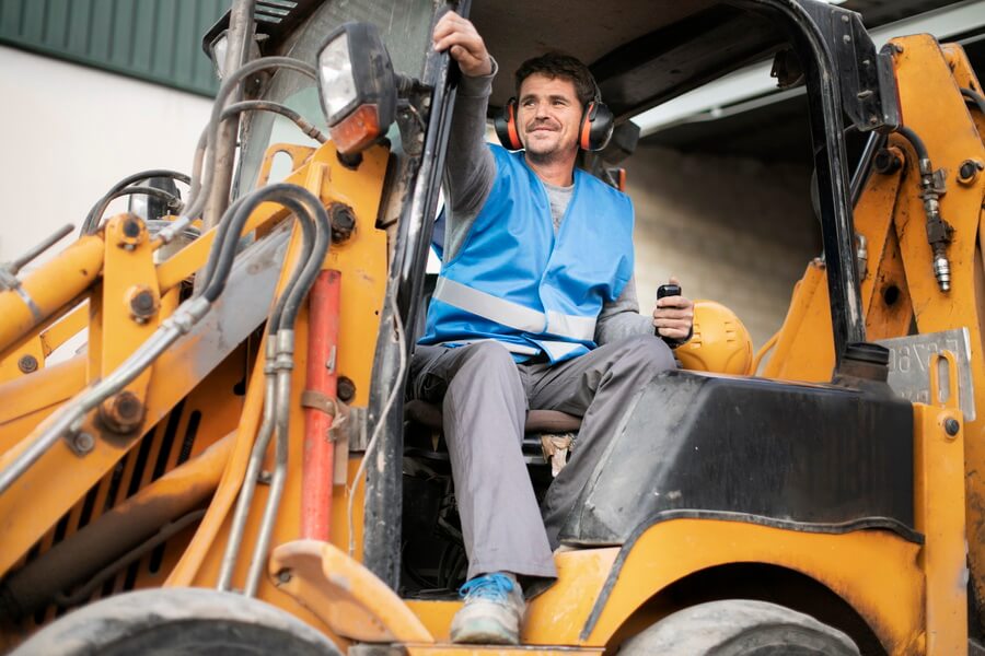 A mobile crane operator at the controls on a construction site — running the machine requires both a current national certification and the employer's documented evaluation on that specific equipment