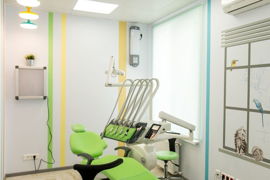 Clean, empty dental operatory with a green patient chair, instrument tray and overhead light in a bright clinic room