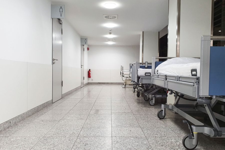 Bright, empty hospital corridor with a row of made-up hospital beds lined along the wall