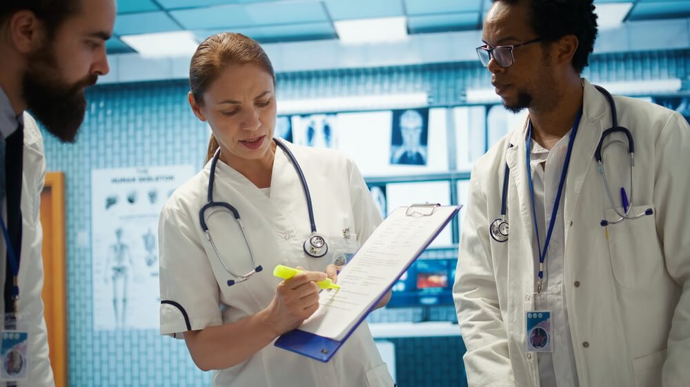 A commercial truck driver handing a medical examiner's certificate to a fleet safety manager reviewing renewal dates on a laptop