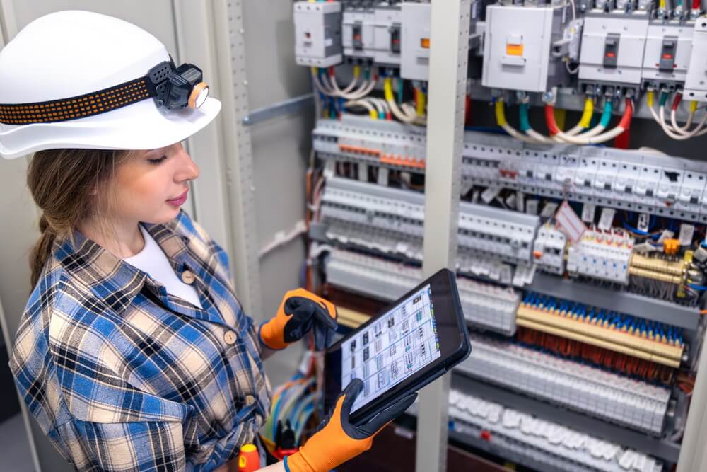 A licensed electrician working on a panel while the office tracks every crew member's license tier and continuing education renewal date