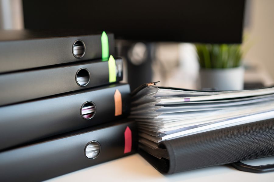 Stack of black ring binders with coloured tabs beside an open document folder on a desk