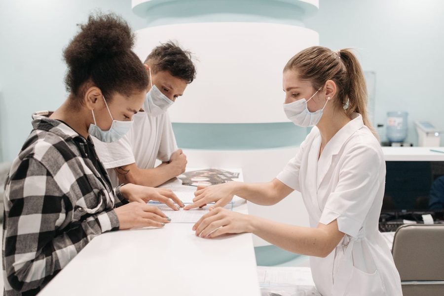 Clinic staff in masks reviewing a desk calendar with visitors at reception