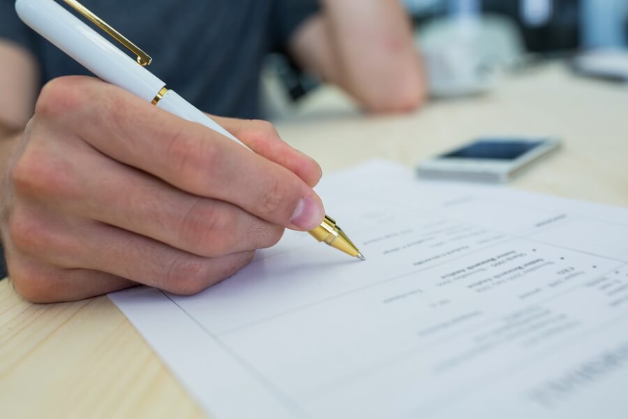 Close-up of a hand completing a printed form at a desk - the annual return a tax-exempt organization owes is straightforward to complete, and the risk lies in the years nobody sits down to do it
