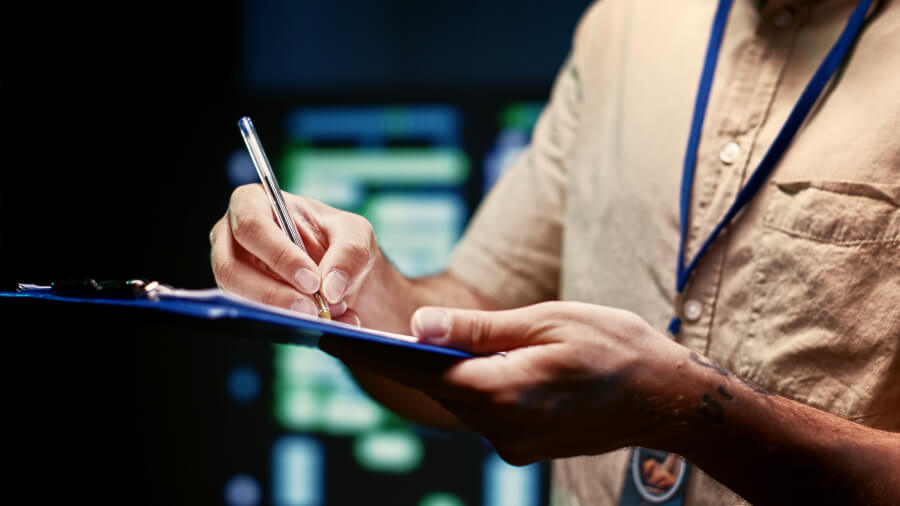 A badged inspector writing findings on a clipboard inside a plant - the daily in-establishment verification a Grant of Inspection rests on