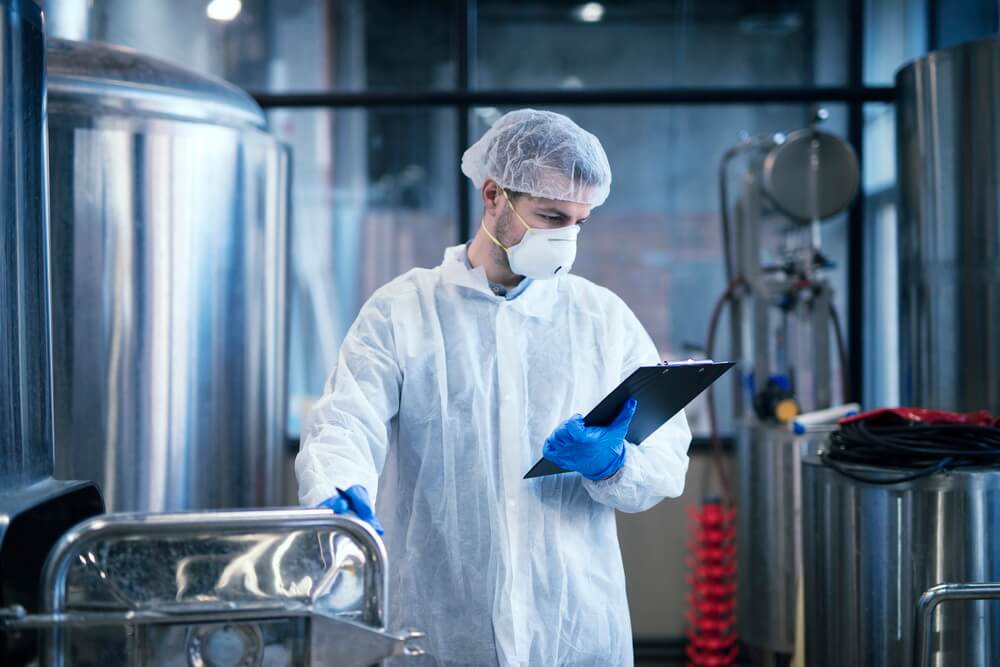 A supplement and food manufacturing facility beside a laptop tracking the annual GMP audit and certificate renewal cycle
