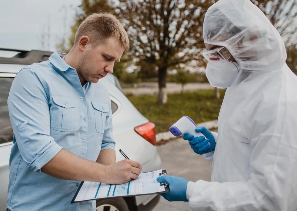 A worker in a full hazmat suit, respirator, and gloves holding a clipboard while a colleague signs a form — the hazardous-materials operations HAZWOPER training qualifies workers to do safely