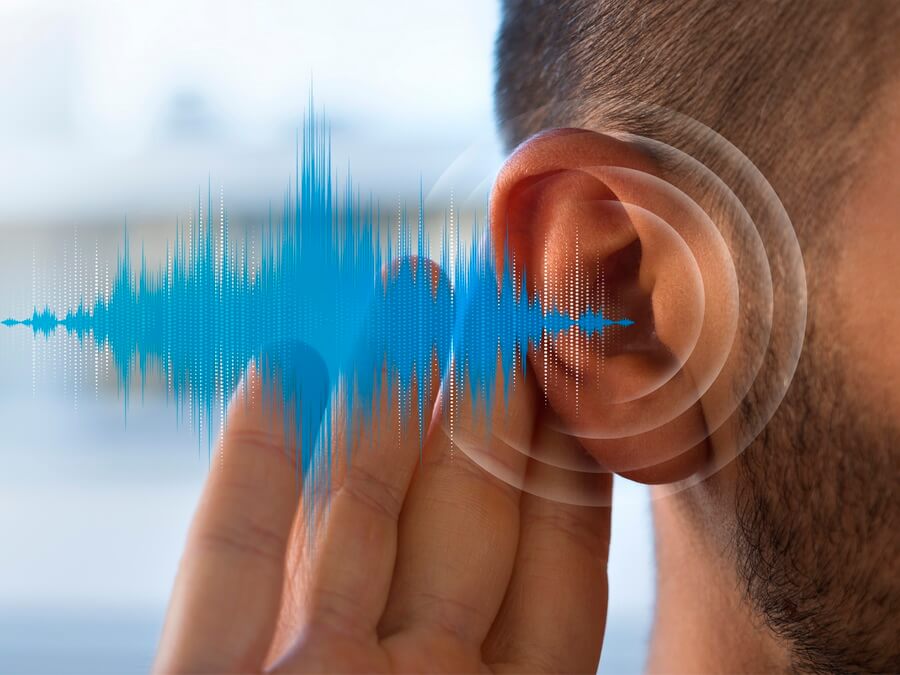 A blue sound waveform meeting a man's ear as he cups a hand behind it — a hearing conservation program measures each covered employee's hearing over time against their preserved baseline audiogram