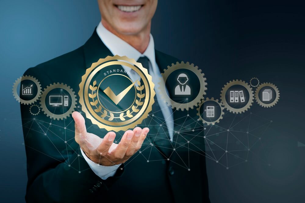 An ISO 9001 certificate beside a laptop tracking the annual surveillance-audit and recertification dates hidden inside its three-year term