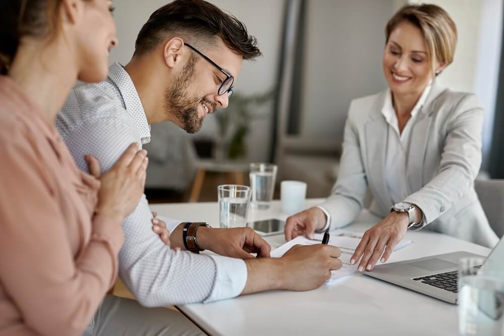Borrowers signing loan paperwork across the desk from their lender — the credit agreement that sets every covenant test date and certificate deadline that follows