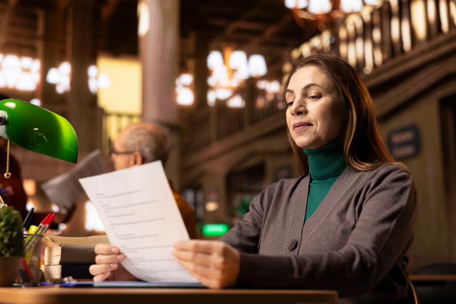 A mortgage loan originator reading a loan document at her desk, while the NMLS renewal window and the annual continuing education deadline that gates it run down unseen