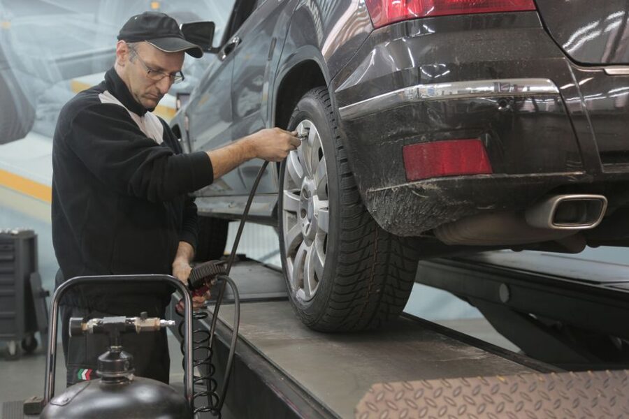 Mechanic in a garage bay checking the tyre of a vehicle raised on a lift with an air line
