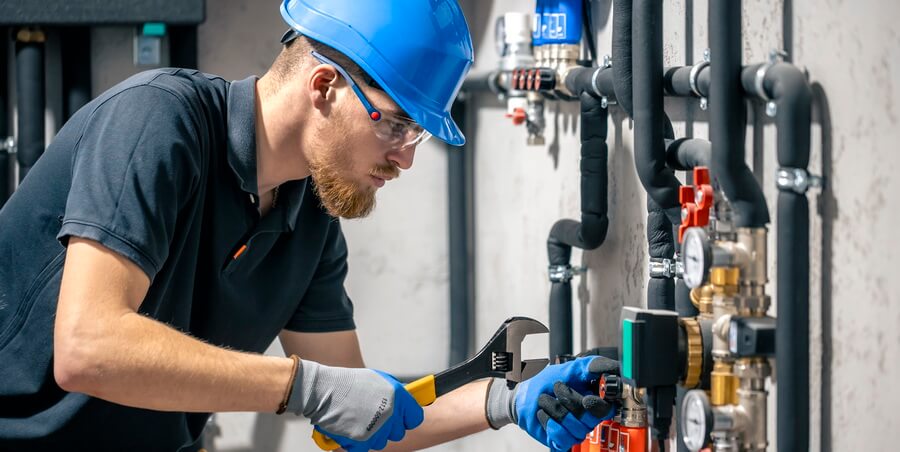 A licensed plumber testing a backflow prevention assembly with a calibrated test gauge while the office tracks the license renewal, tester certification, and annual test dates