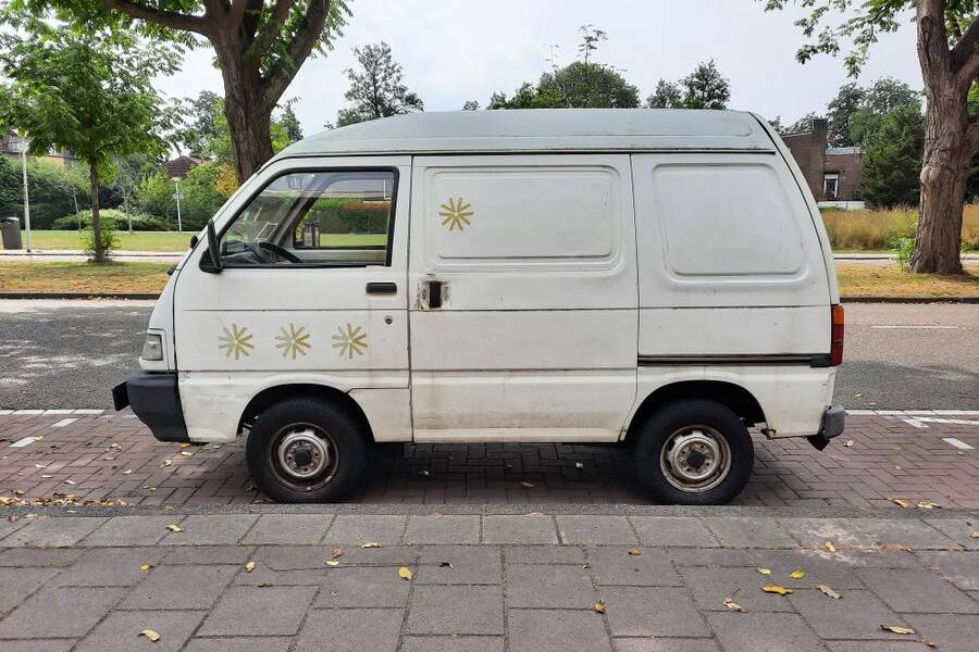 Older white van parked at the kerb of a tree-lined street with paving beside it