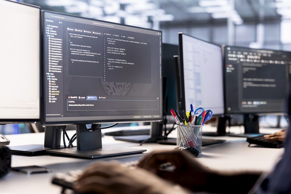 Developer workstations with code on screen in an office — software and SaaS licenses that renew on their own terms and can lapse or auto-renew