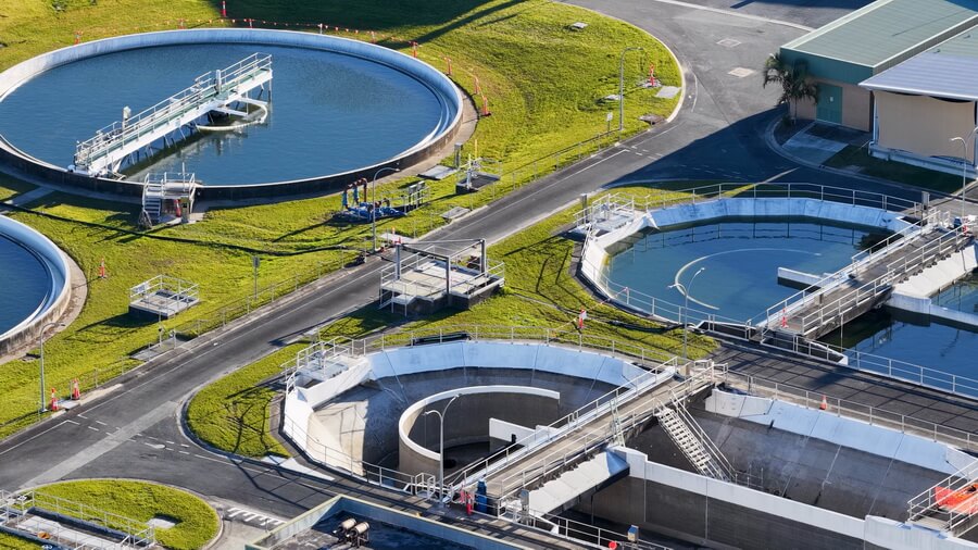 A certified operator checking treatment equipment at a water facility while the utility tracks every operator's certification grade and continuing education against each facility's required grade
